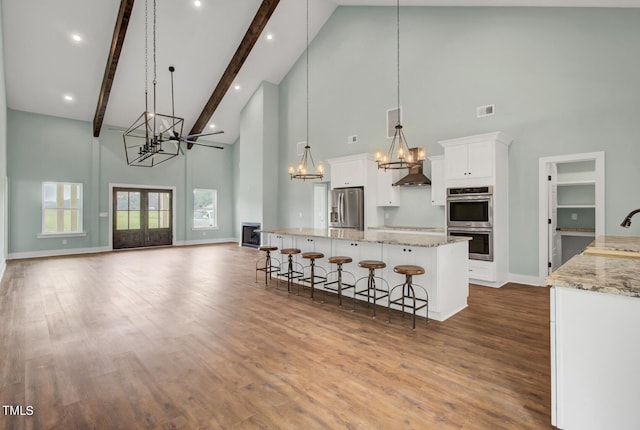 kitchen with stainless steel appliances, white cabinets, decorative light fixtures, wood-type flooring, and high vaulted ceiling