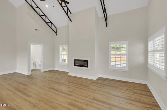 unfurnished living room featuring ceiling fan, a high ceiling, and light hardwood / wood-style floors