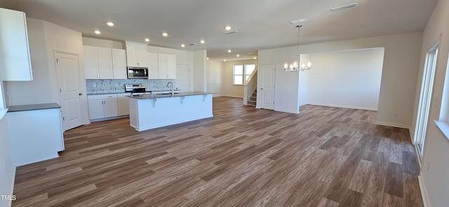 kitchen with a center island with sink, wood-type flooring, appliances with stainless steel finishes, white cabinets, and an inviting chandelier