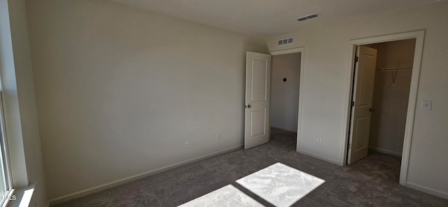 unfurnished bedroom with a spacious closet, a closet, and dark carpet