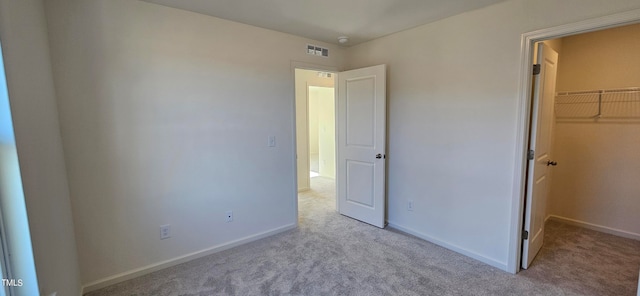 unfurnished bedroom featuring a walk in closet, a closet, and light carpet