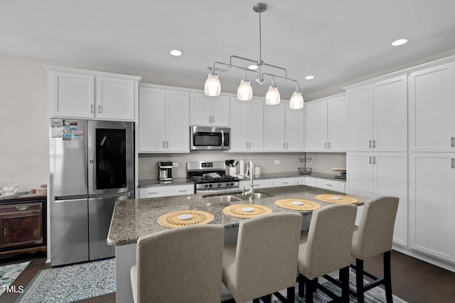 kitchen with stone counters, a kitchen island with sink, dark wood-type flooring, white cabinets, and appliances with stainless steel finishes