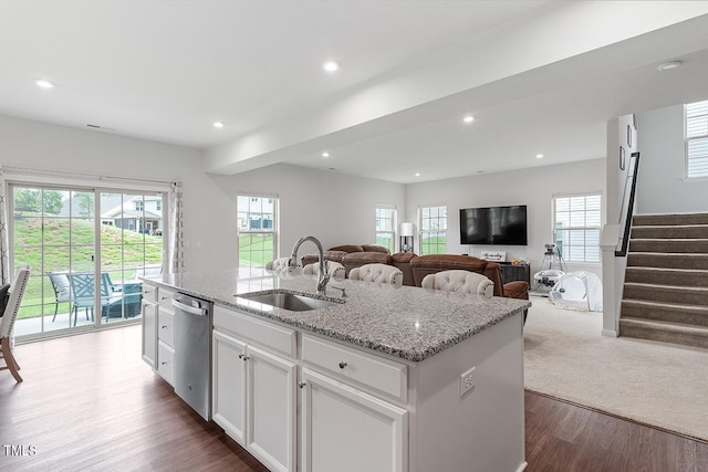 kitchen with dishwasher, sink, white cabinetry, hardwood / wood-style flooring, and a kitchen island with sink