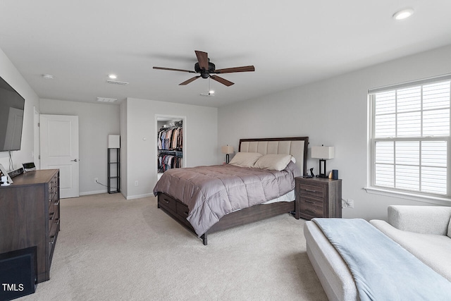 bedroom featuring light carpet, a walk in closet, a closet, and ceiling fan