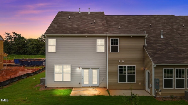 back house at dusk featuring a patio, a yard, and central AC unit