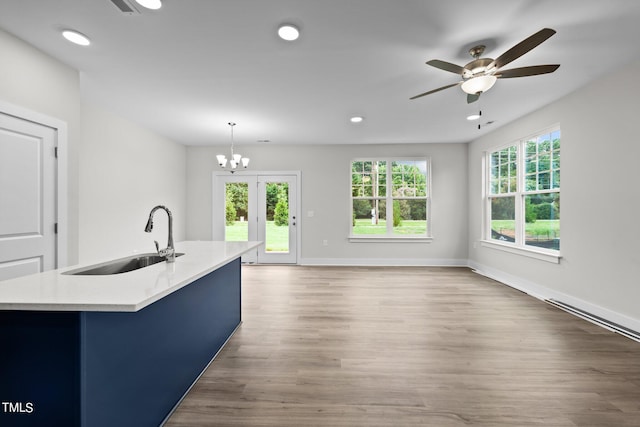 kitchen with sink, wood-type flooring, decorative light fixtures, an island with sink, and ceiling fan with notable chandelier