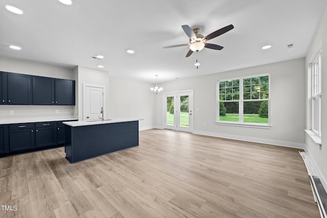 kitchen featuring ceiling fan with notable chandelier, sink, hanging light fixtures, a kitchen island with sink, and light wood-type flooring