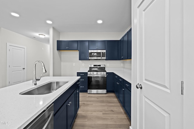 kitchen featuring blue cabinetry, sink, appliances with stainless steel finishes, light stone countertops, and light hardwood / wood-style floors