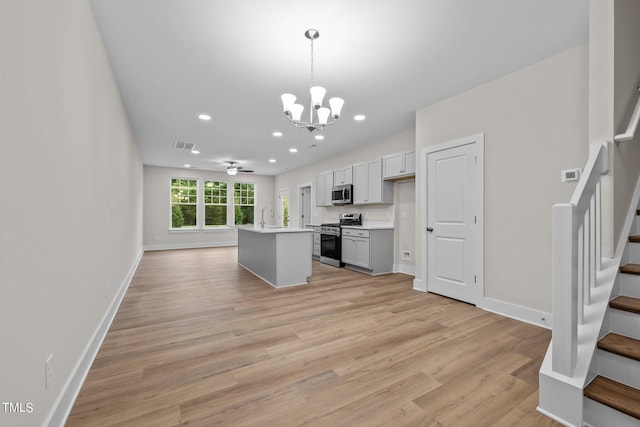 kitchen featuring decorative light fixtures, light hardwood / wood-style floors, a kitchen island with sink, stainless steel appliances, and ceiling fan with notable chandelier