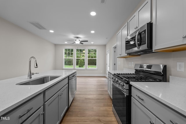 kitchen with sink, light stone counters, light wood-type flooring, gray cabinets, and stainless steel appliances