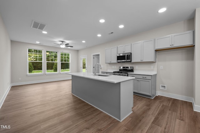 kitchen with sink, appliances with stainless steel finishes, gray cabinetry, hardwood / wood-style floors, and an island with sink