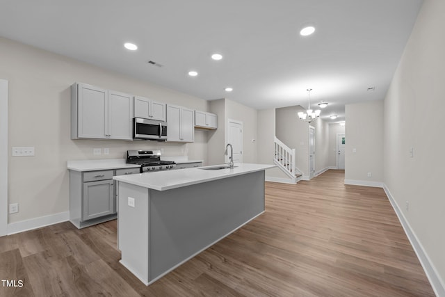 kitchen with stainless steel appliances, light wood-type flooring, a center island with sink, and gray cabinetry