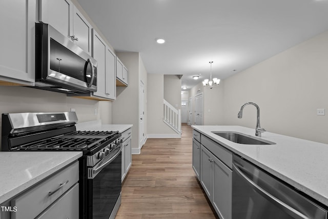 kitchen with appliances with stainless steel finishes, sink, hanging light fixtures, light stone countertops, and light wood-type flooring