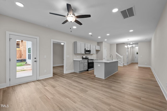 kitchen featuring pendant lighting, gray cabinets, stainless steel appliances, light hardwood / wood-style floors, and a center island with sink