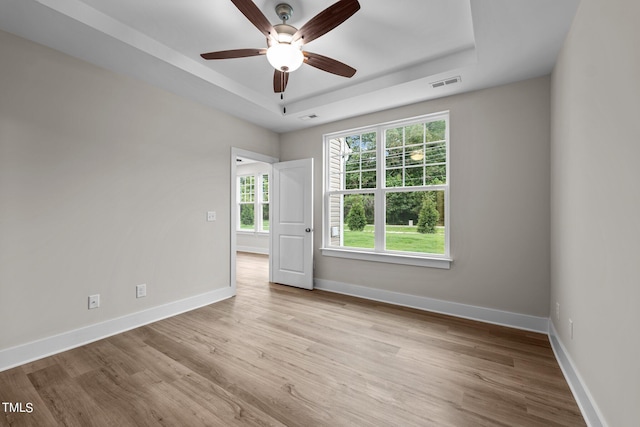 spare room with ceiling fan, a tray ceiling, and light wood-type flooring