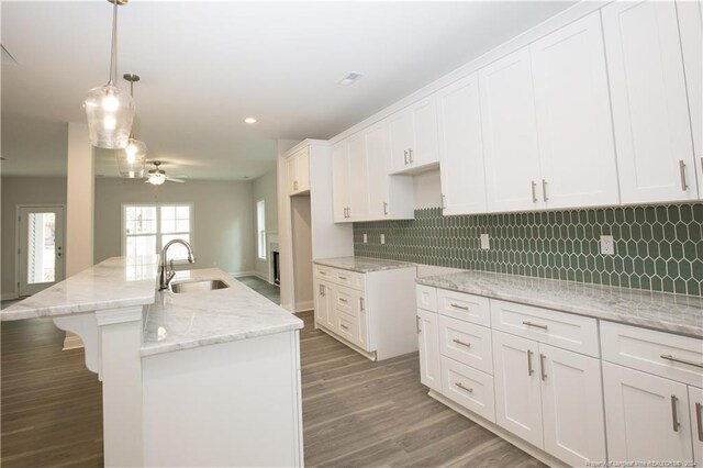 kitchen featuring ceiling fan, sink, wood-type flooring, pendant lighting, and a center island with sink