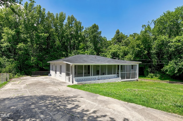 view of front of house featuring driveway, a front yard, fence, and a sunroom