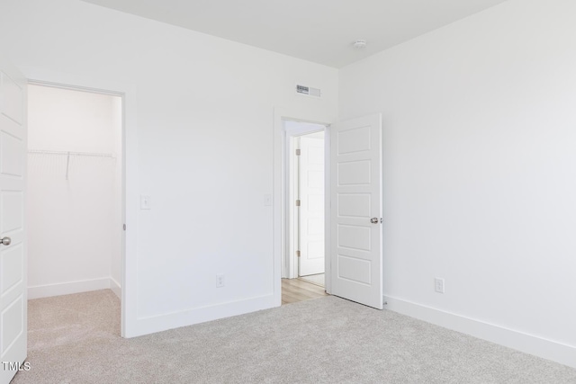 unfurnished bedroom featuring a walk in closet, a closet, and light colored carpet