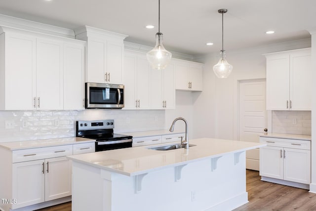 kitchen with appliances with stainless steel finishes, sink, pendant lighting, a center island with sink, and white cabinets