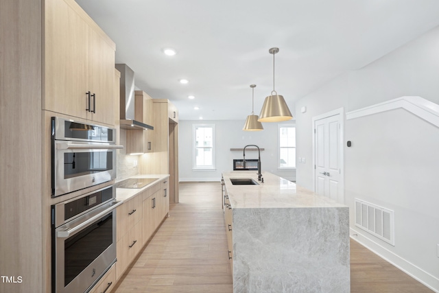 kitchen with light brown cabinetry, light hardwood / wood-style floors, sink, and wall chimney range hood