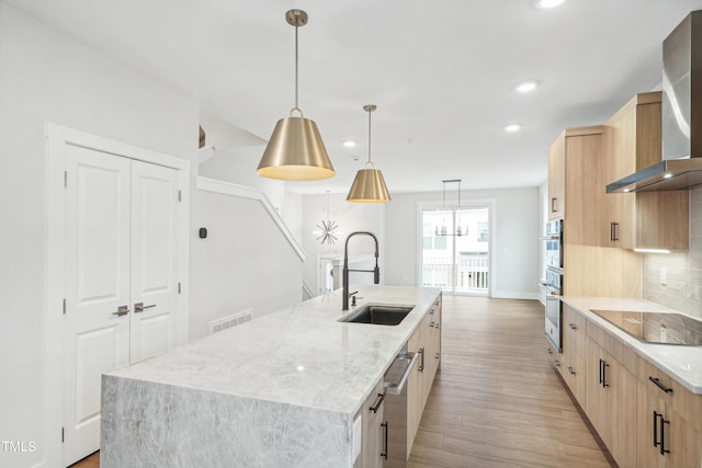 kitchen featuring hanging light fixtures, stainless steel appliances, light brown cabinetry, a center island with sink, and sink