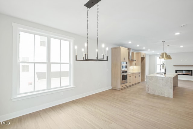 kitchen with light brown cabinets, hanging light fixtures, sink, a kitchen island with sink, and light hardwood / wood-style floors