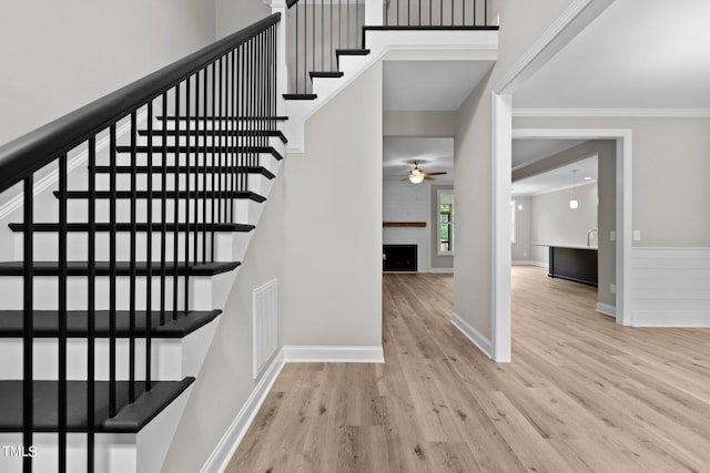 stairs with ceiling fan, crown molding, and wood-type flooring