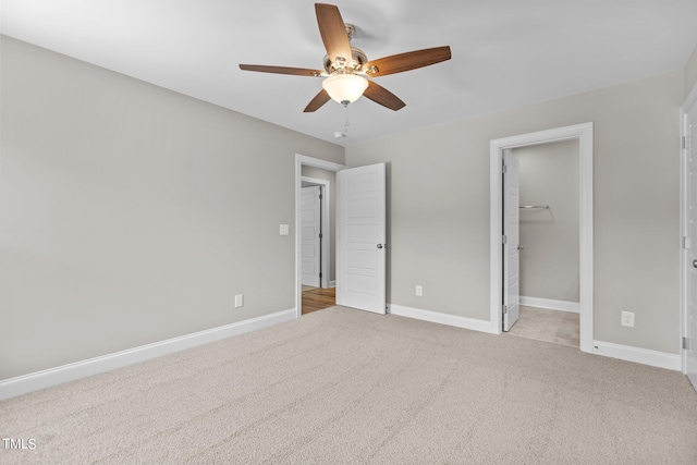 unfurnished bedroom with light colored carpet, a walk in closet, and ceiling fan