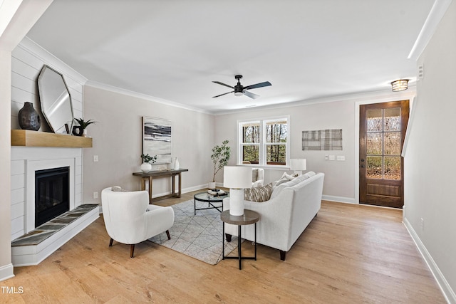 living area featuring baseboards, light wood-type flooring, a fireplace, and crown molding