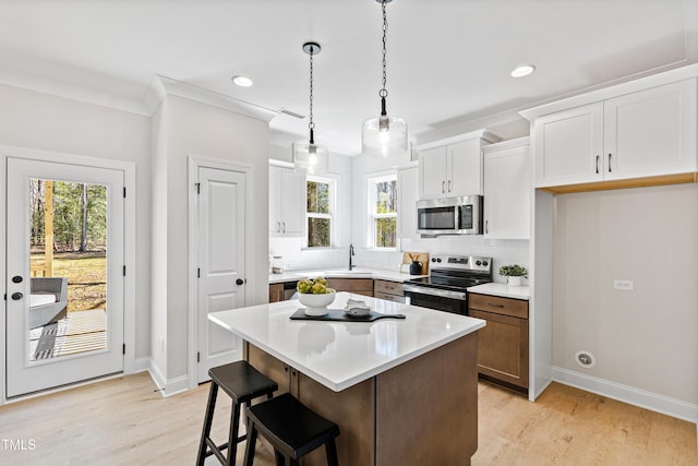 kitchen with a center island, decorative light fixtures, light countertops, appliances with stainless steel finishes, and white cabinetry