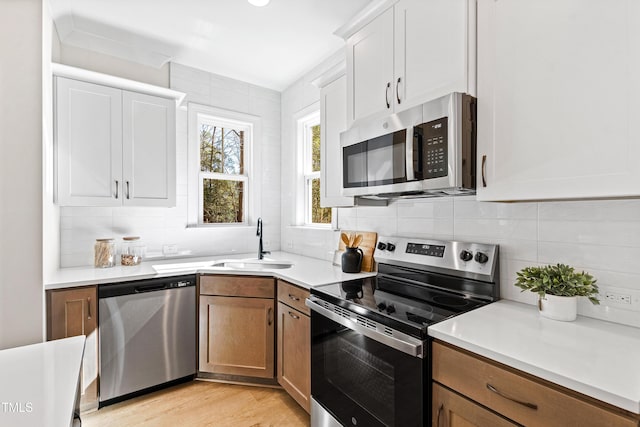 kitchen featuring stainless steel appliances, light countertops, brown cabinetry, white cabinetry, and a sink