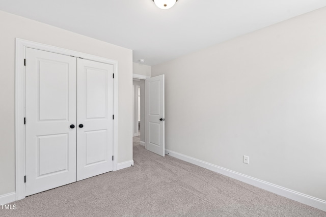 unfurnished bedroom with baseboards, a closet, and light colored carpet