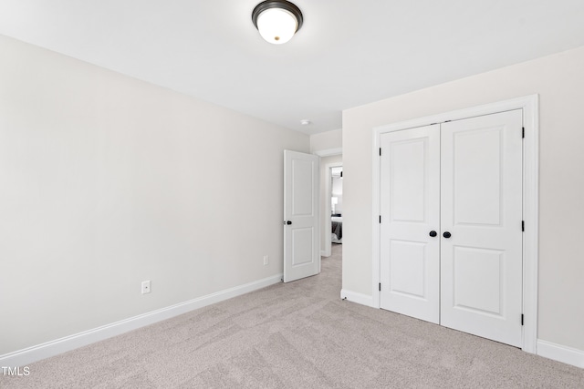 unfurnished bedroom featuring a closet, light colored carpet, and baseboards