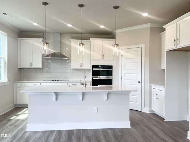 kitchen with light countertops, tasteful backsplash, ornamental molding, and wall chimney range hood
