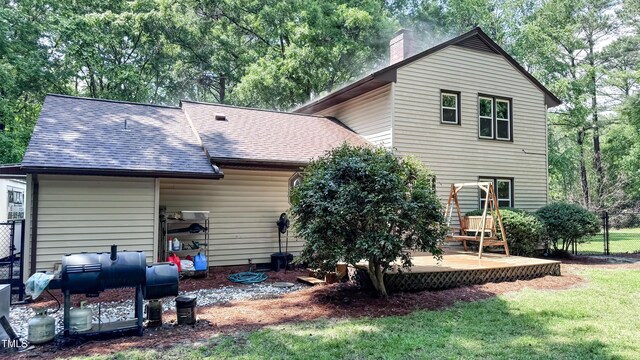 back of house with a chimney, a shingled roof, and view of scattered trees