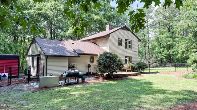 back of house featuring roof with shingles, a chimney, a patio area, and view of wooded area