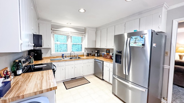 kitchen featuring appliances with stainless steel finishes, a sink, ornamental molding, light flooring, and white cabinets