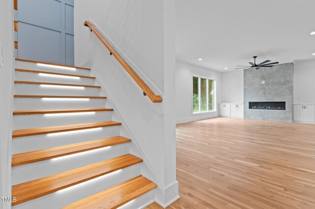 stairs featuring ceiling fan, a fireplace, and hardwood / wood-style floors