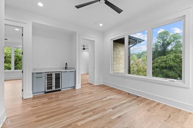 bar featuring ceiling fan, beverage cooler, crown molding, sink, and light hardwood / wood-style flooring