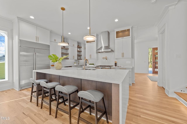 kitchen with appliances with stainless steel finishes, white cabinetry, a wealth of natural light, and wall chimney range hood