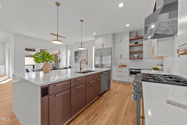 kitchen featuring premium appliances, a kitchen island with sink, sink, wall chimney range hood, and white cabinets