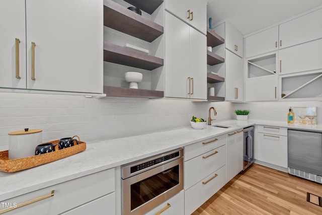 kitchen with white cabinetry, light wood-type flooring, light stone countertops, and sink