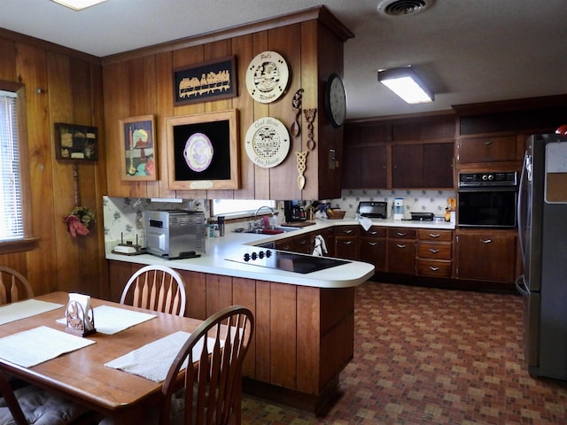 kitchen featuring wood walls, kitchen peninsula, black appliances, and dark tile floors