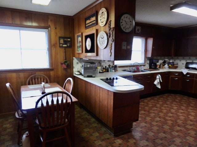 kitchen featuring kitchen peninsula, backsplash, wood walls, sink, and dark tile flooring