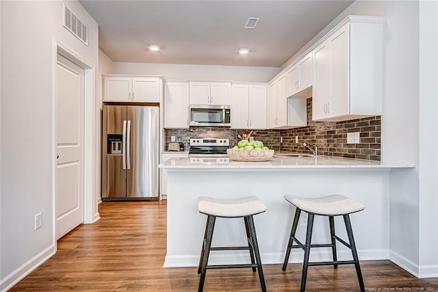 kitchen featuring kitchen peninsula, white cabinetry, stainless steel appliances, and light wood-type flooring