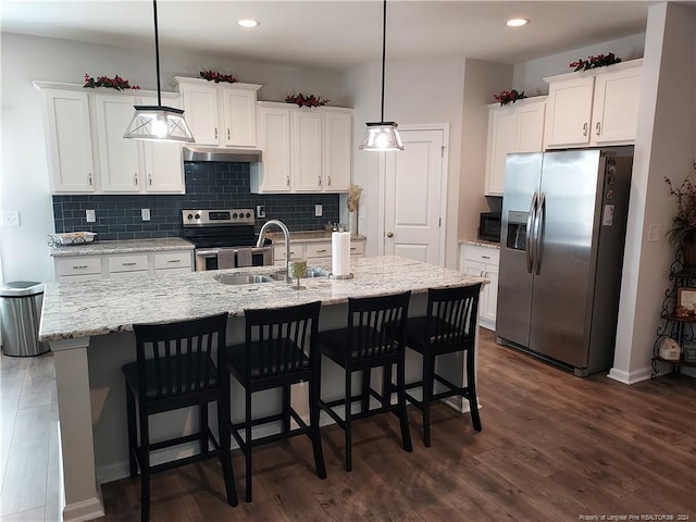 kitchen featuring appliances with stainless steel finishes, a sink, under cabinet range hood, white cabinets, and tasteful backsplash
