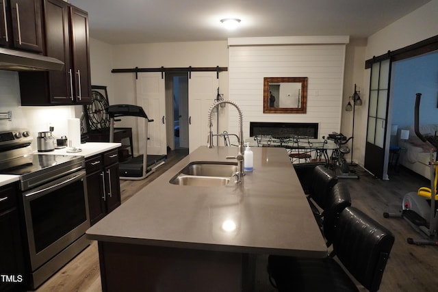 kitchen with a barn door, stainless steel electric range oven, an island with sink, and sink