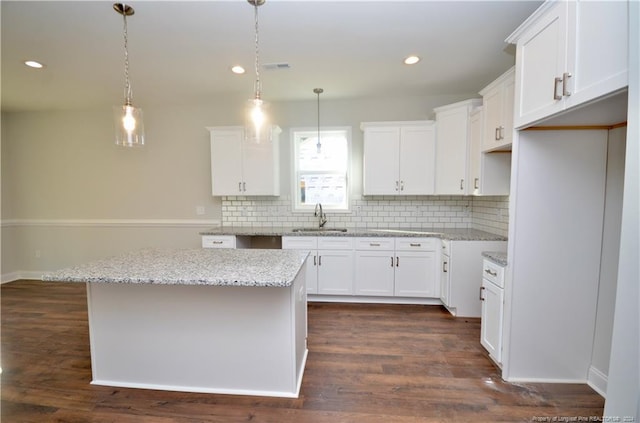 kitchen featuring light stone countertops, a center island, pendant lighting, white cabinets, and dark hardwood / wood-style floors