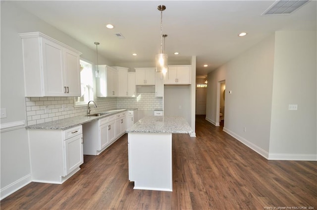 kitchen with dark wood-type flooring, sink, light stone countertops, a center island, and white cabinetry