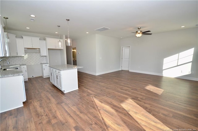 kitchen featuring a kitchen island, white cabinetry, light stone countertops, dark wood-type flooring, and sink